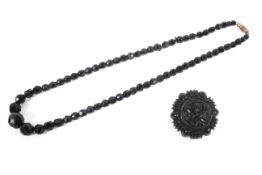 A jet carved brooch together with black graduated necklace.