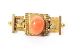 An unmarked yellow metal Etruscan style brooch set with central oval pink coral cabochon. 4.5g.