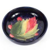 A small Moorcroft dish in leaf and berries pattern reserved on a dark blue ground, 20th century,