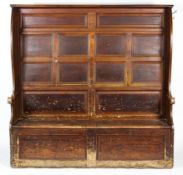 A 19th century oak settle, with panelled back above two hinged cupboard doors, with scroll arms,