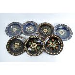 Seven French slip glazed stoneware plates with a central flower on a brown and blue ground,