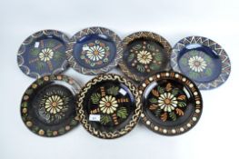 Seven French slip glazed stoneware plates with a central flower on a brown and blue ground,