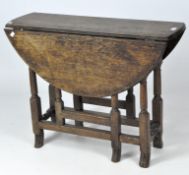 An oak drop leaf table in the 17th century style, with circular top on turned legs and paw feet,