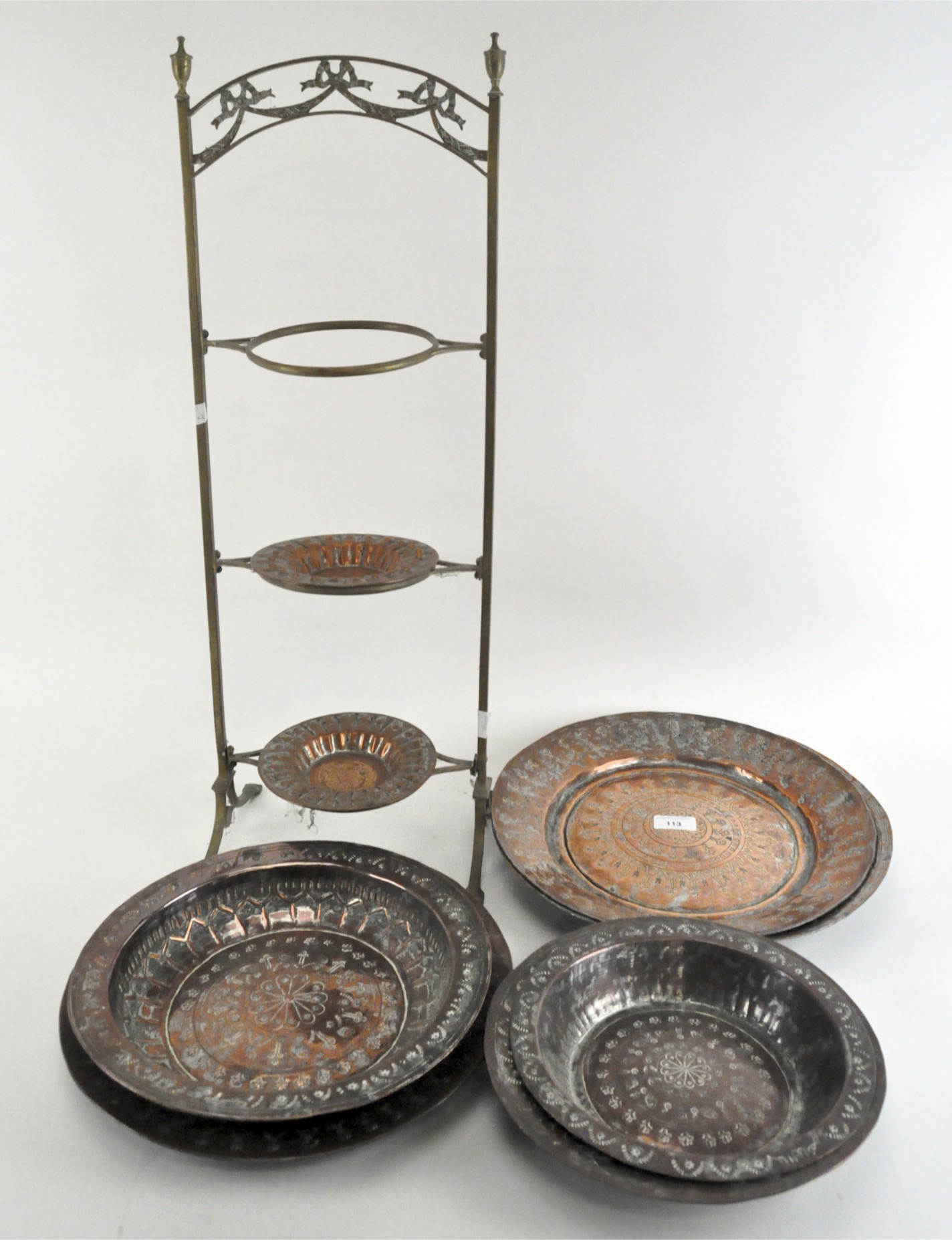 A three-tier plate stand with a metal frame together with a selection of engraved copper plates