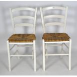 A pair of white painted dining chairs, with wicker seats,