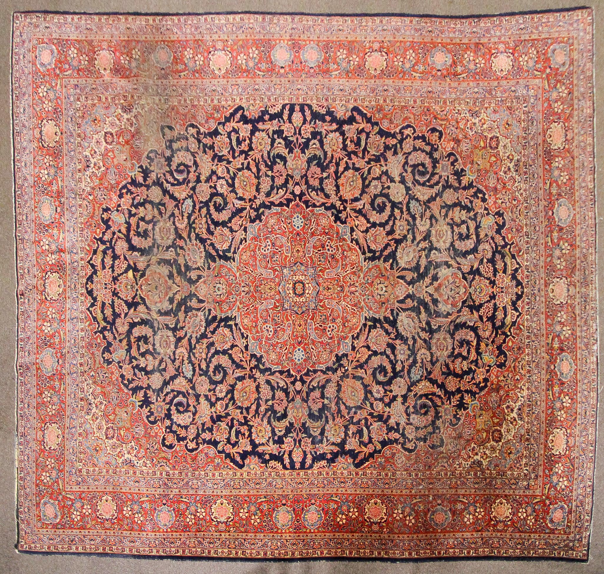 A large Persian silk/wool rug red ground with central floral panel and three floral; borders.