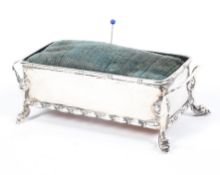 An Edwardian silver pin cushion of rectangular form, twin handled and raised upon scrolling feet,