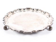 An Edwardian silver salver, having pie crust border, raised upon three scrolling feet,