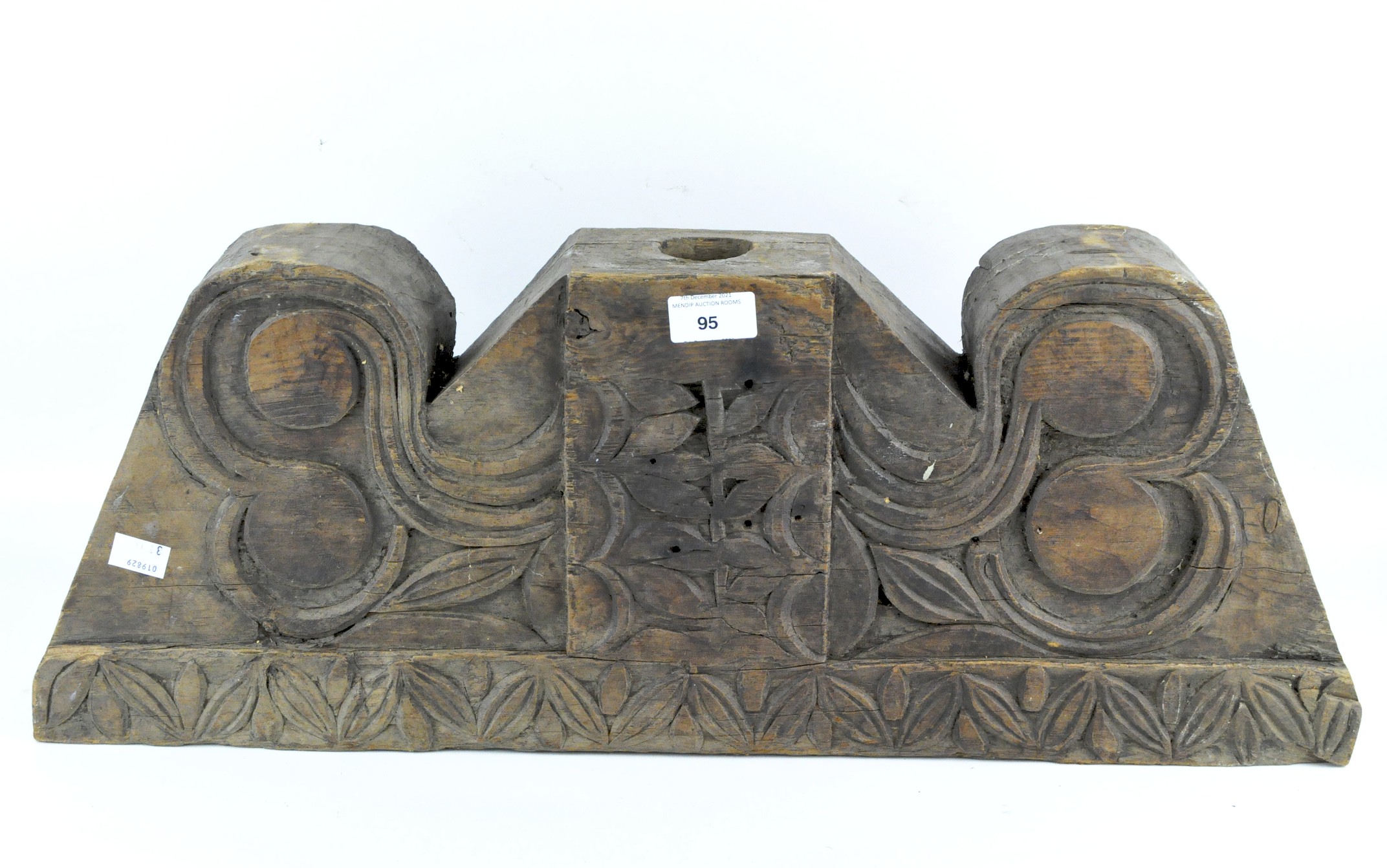 A trapezoid shaped wooden architectural frament carved to one side with leaves and volutes,