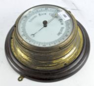 A circular wall barometer, white dial mounted in brass on a wooden plaque,