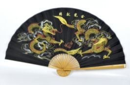 A large contemporary folding fan, wooden guards and stick with a fabric leaf decorated with dragons,