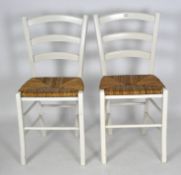 A pair of white painted dining chairs, with wicker seats,