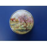 An enamelled circular silver pill box, the hinged cover painted to show sheep grazing in an