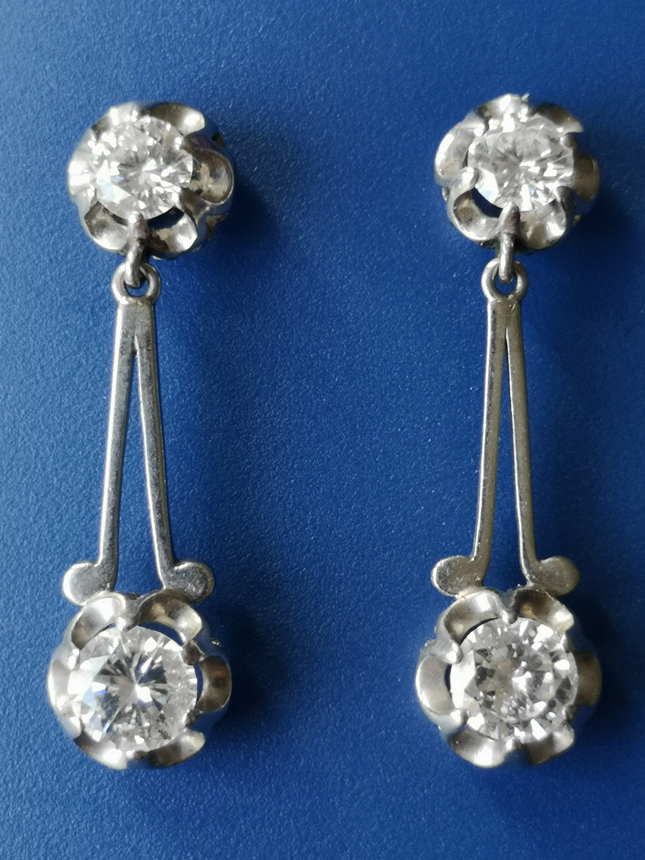 A pair of diamond set white metal drop earrings, each having two claw set brilliant cut stones,