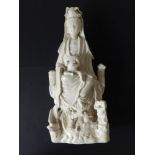 A large early Chinese blanc de chine porcelain figure of a seated Kuan Yin with two small dragons at