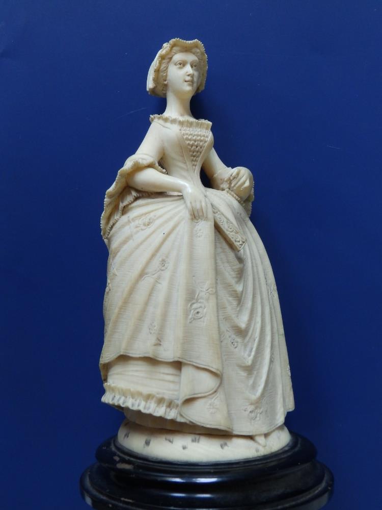 An antique carved ivory female figure, depicting a young woman in 18thC costume, holding a fan in