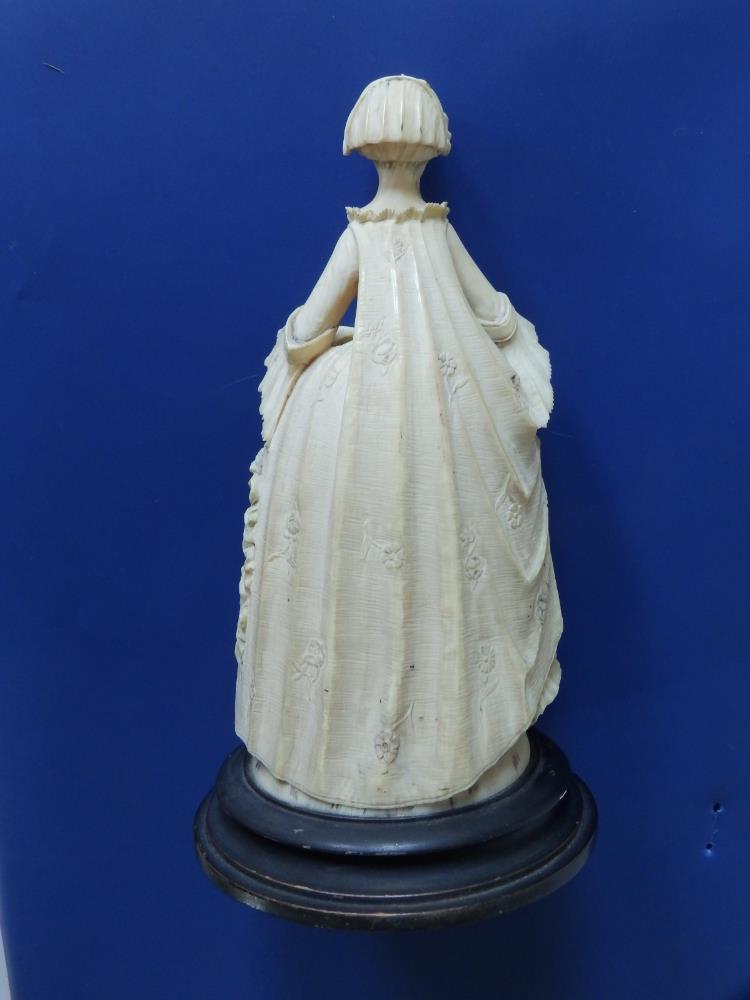 An antique carved ivory female figure, depicting a young woman in 18thC costume, holding a fan in - Image 4 of 6