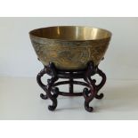 A Chinese brass bowl decorated with dragons, phoenix and a fish, 9.5" diameter on wooden stand,