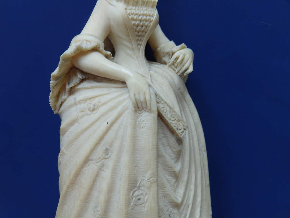 An antique carved ivory female figure, depicting a young woman in 18thC costume, holding a fan in - Image 3 of 6