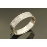 A silver foliate engraved bangle, with safety chain.