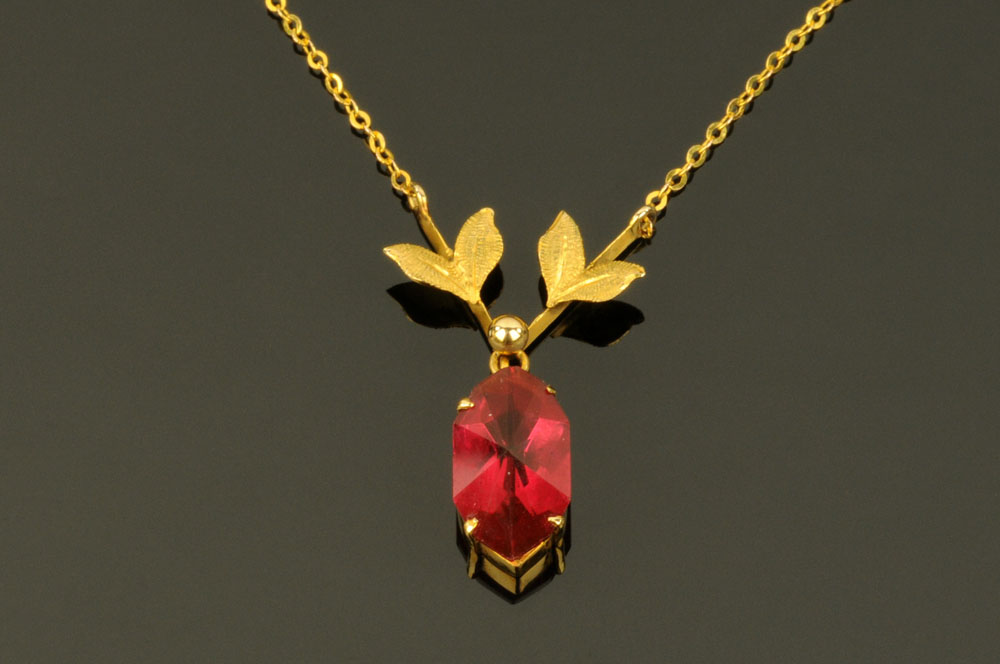 A 9 ct gold leaf shaped pendant and chain, with ruby coloured stone.