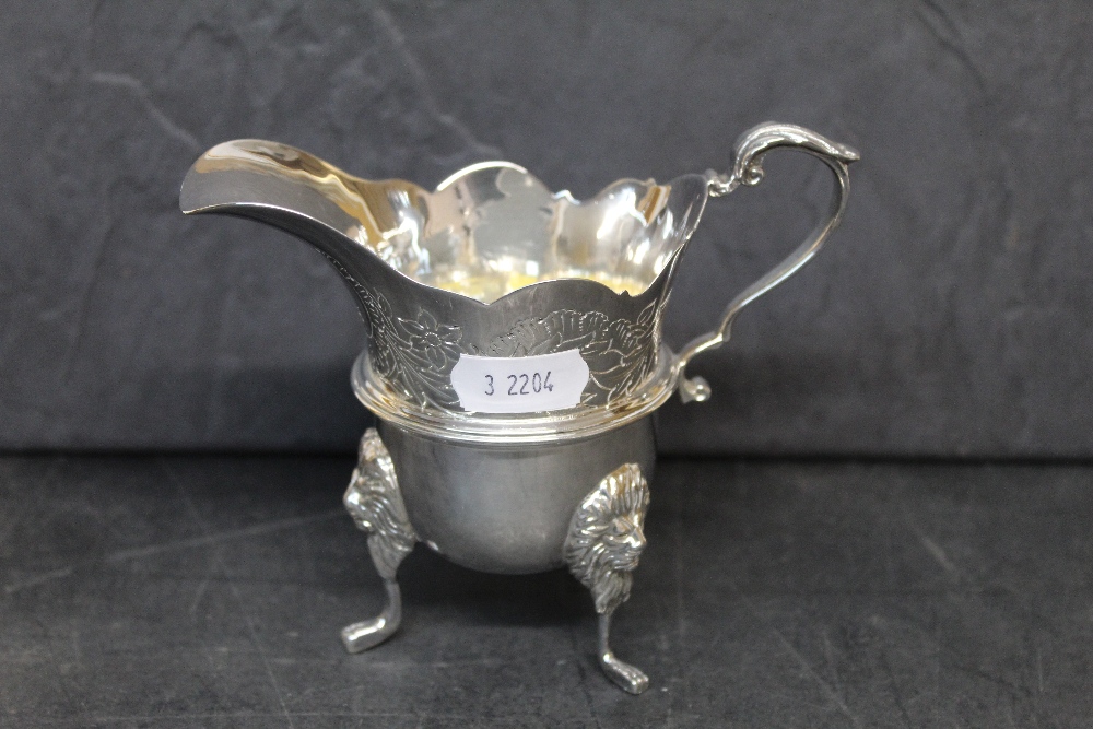 An Elizabeth II silver cream jug of George II design with pronounced spout, engraved with leaves,