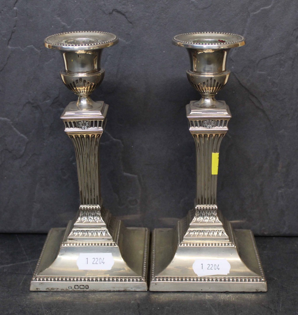 A pair of late Victorian silver pillar candlesticks of reeded column design on square bases,