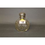 A silver topped cut glass scent bottle of globular form with scrolled embossed cover (wear to