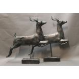 A pair of modern figures of leaping deer, having metal look bodies and mounted on wooden stands.