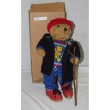 A Lakeland Bears teddy bear, titled "Cragg", wearing a red corduroy cap, black duffel coat,