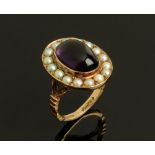 A 9 ct gold ring set with an amethyst coloured cabochon and seed pearl surround. Size M, 8.6 grams.