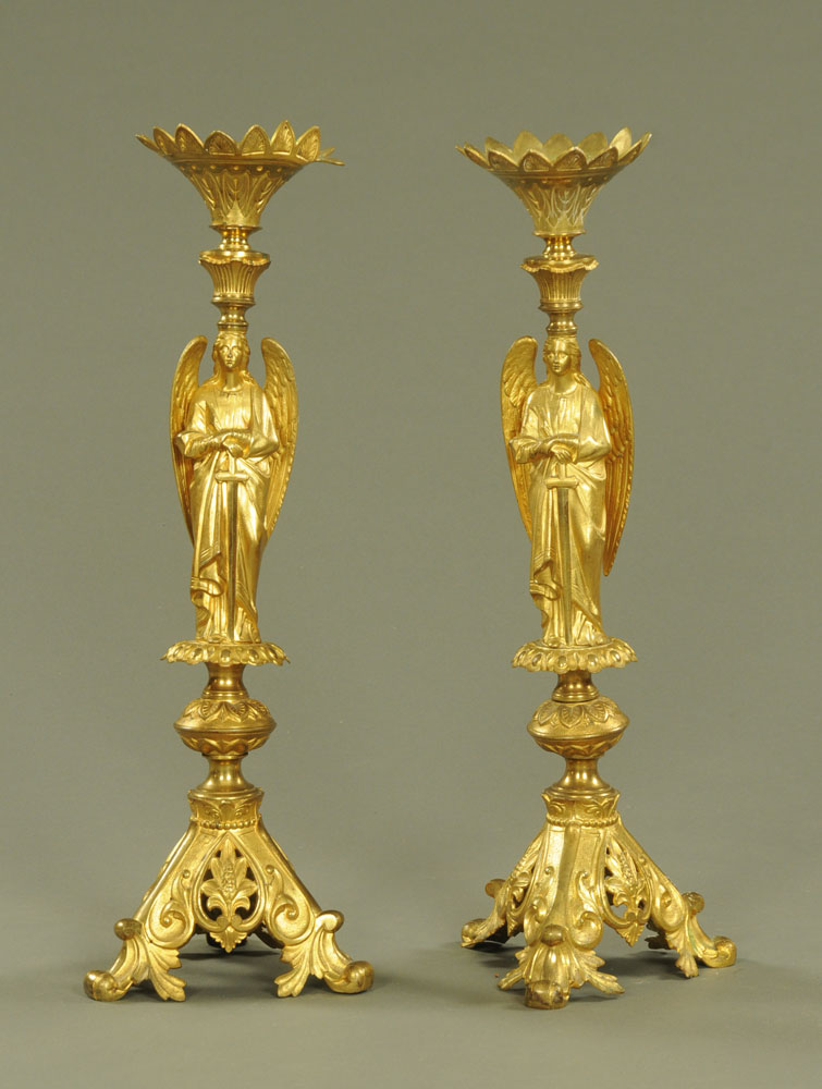 A pair of brass pricket candlesticks, with winged angel supports and raised on three scroll feet.