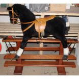 A modern black fur rocking horse, with tan leather bridle, saddle, and stirrups,