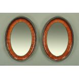 A pair of 1920's grained wood and ebonised oval wall mirrors with bevelled plates. 86 cm x 59 cm.