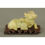 A Chinese carved jade water buffalo, on wooden stand. Length 23 cm.