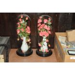 Two vases of artificial flowers on a stand and under glass domes