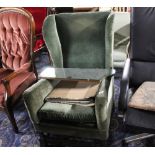 A wing back armchair upholstered in green cloth and having carved oak frame
