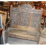 An oak carved settle of 18th century style with lift up seat and measuring 124 cm tall x 102 cm