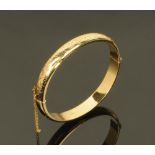 A 9 ct gold foliate engraved bangle, with safety chain, 12.1 grams.