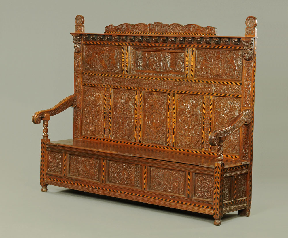 A Victorian carved oak settle, decorated with floral, armorial and religious panels,