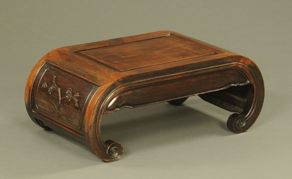 A Chinese hardwood saddle shaped low table, decorated with prunus blossom.
