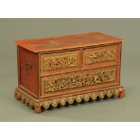 A Chinese red lacquered gilt painted low chest of two short and one long drawer with carved front,