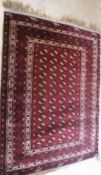 A Bokhara rug, the central panel set with elephant foot medallions on a dark red ground,