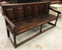 A circa 1900 oak settle, the carved six panel back decorated with flowers in the Aesthetic taste,