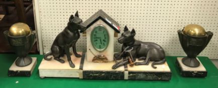 A 1930s marble and onyx cased clock garniture as a dog kennel flanked by two hounds, one seated,