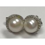 A pair of white metal mounted (indistinctly stamped, probably gold) diamond and pearl ear studs,