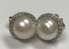 A pair of white metal mounted (indistinctly stamped, probably gold) diamond and pearl ear studs,