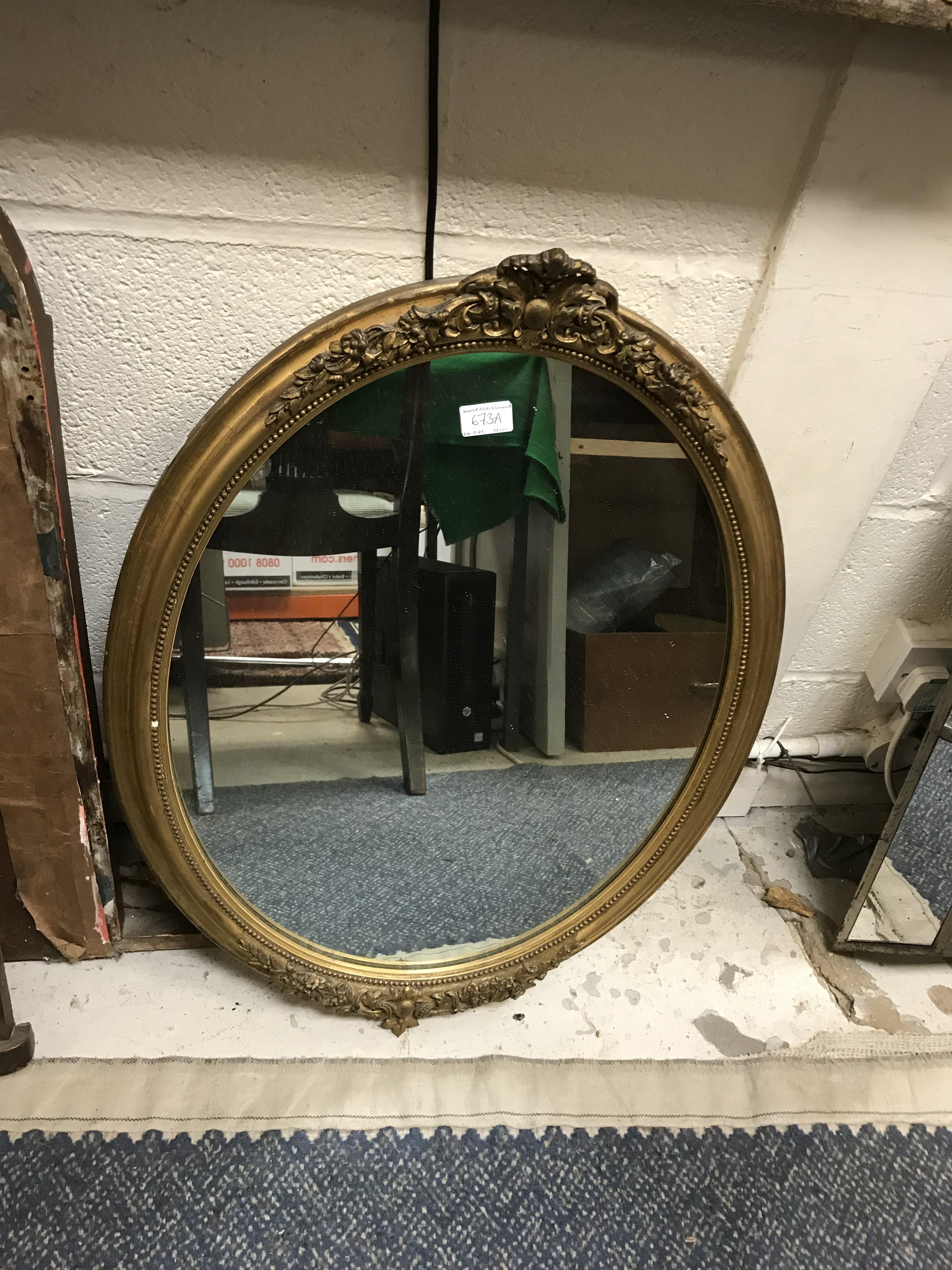 A circa 1900 giltwood and gesso framed oval wall mirror with relief-work decorated surmount and