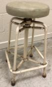A 1950's Cowtan & Cox wrought iron framed adjustable stool on sprung pedestal to splayed legs
