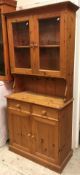 A modern pine dresser with two glazed doors over two drawers and two cupboard doors on a plinth